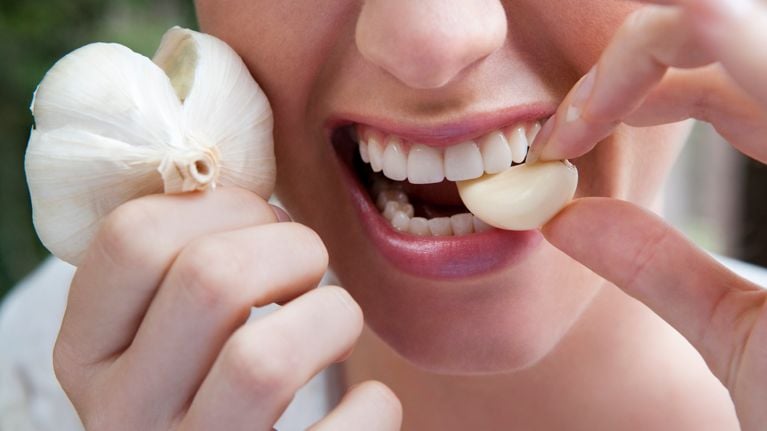 close up of woman biting into a garlic clove
